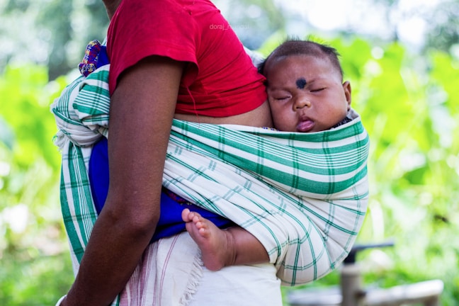 A parent adjusting the straps of a baby carrier while their infant peacefully sleeps inside.