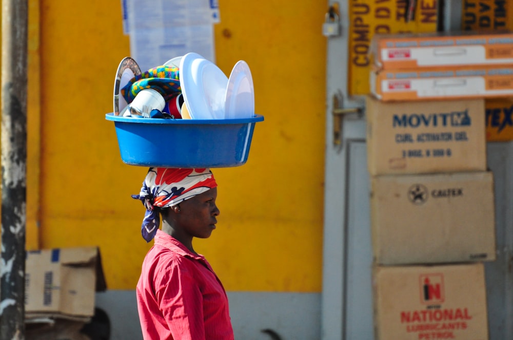 woman in red collared top carrying basin on head