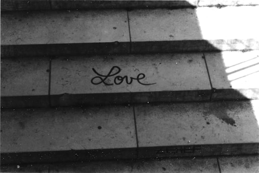 A set of concrete steps with shadows cast diagonally across them. The word 'Love' is written on one of the steps in a cursive style. The surface shows signs of wear and has some stains.