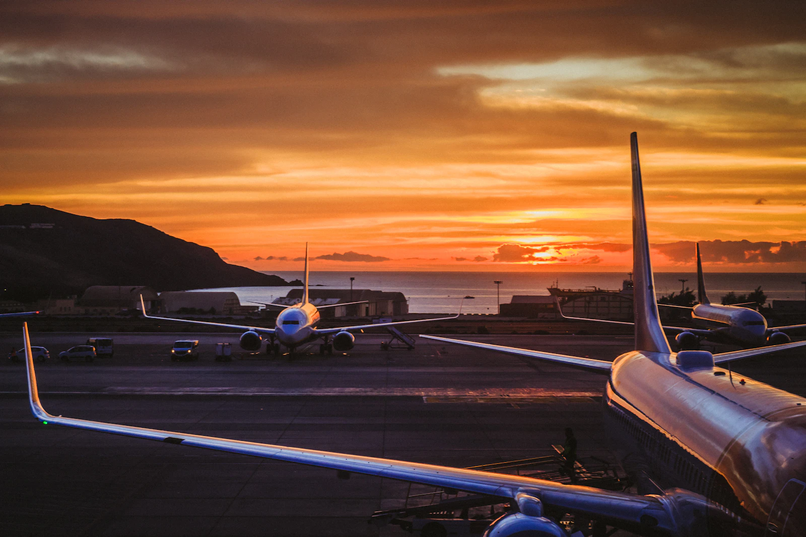 Photograph showing three passenger aircraft stand on an airport apron beneath an orange sunrise.