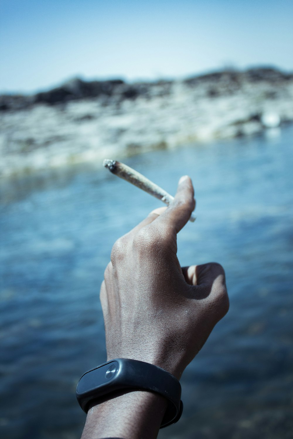 a hand holding a cigarette in front of a body of water