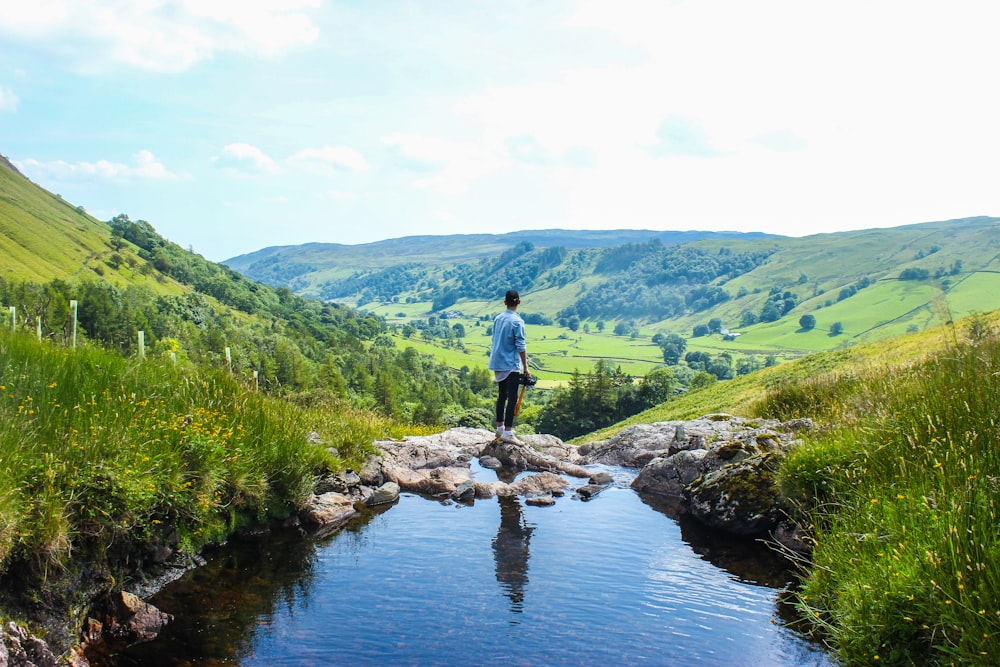 man standing on river near mountain range