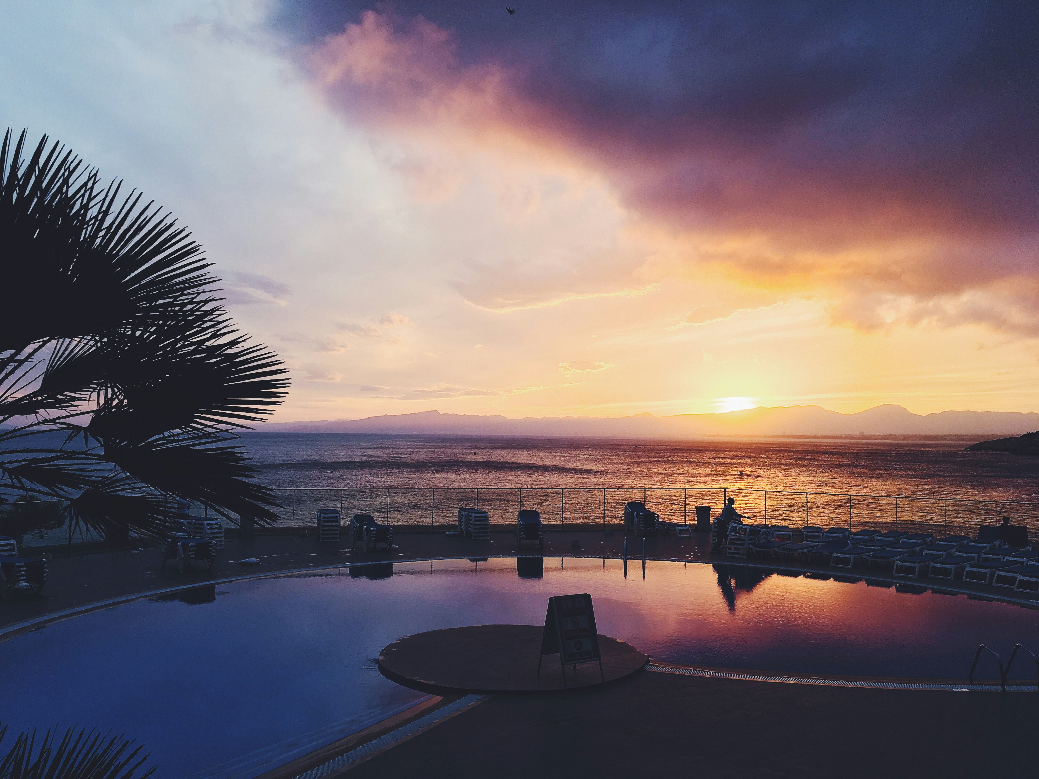 A vibrant sunset casting colors over a tranquil resort pool.