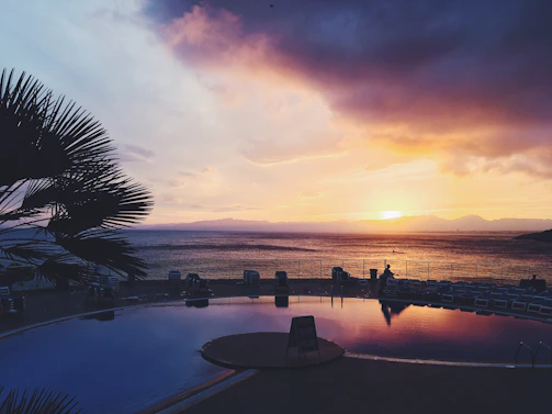 Sunset over a serene countryside villa pool, the sky painted in warm bronze and deepening blue hues.