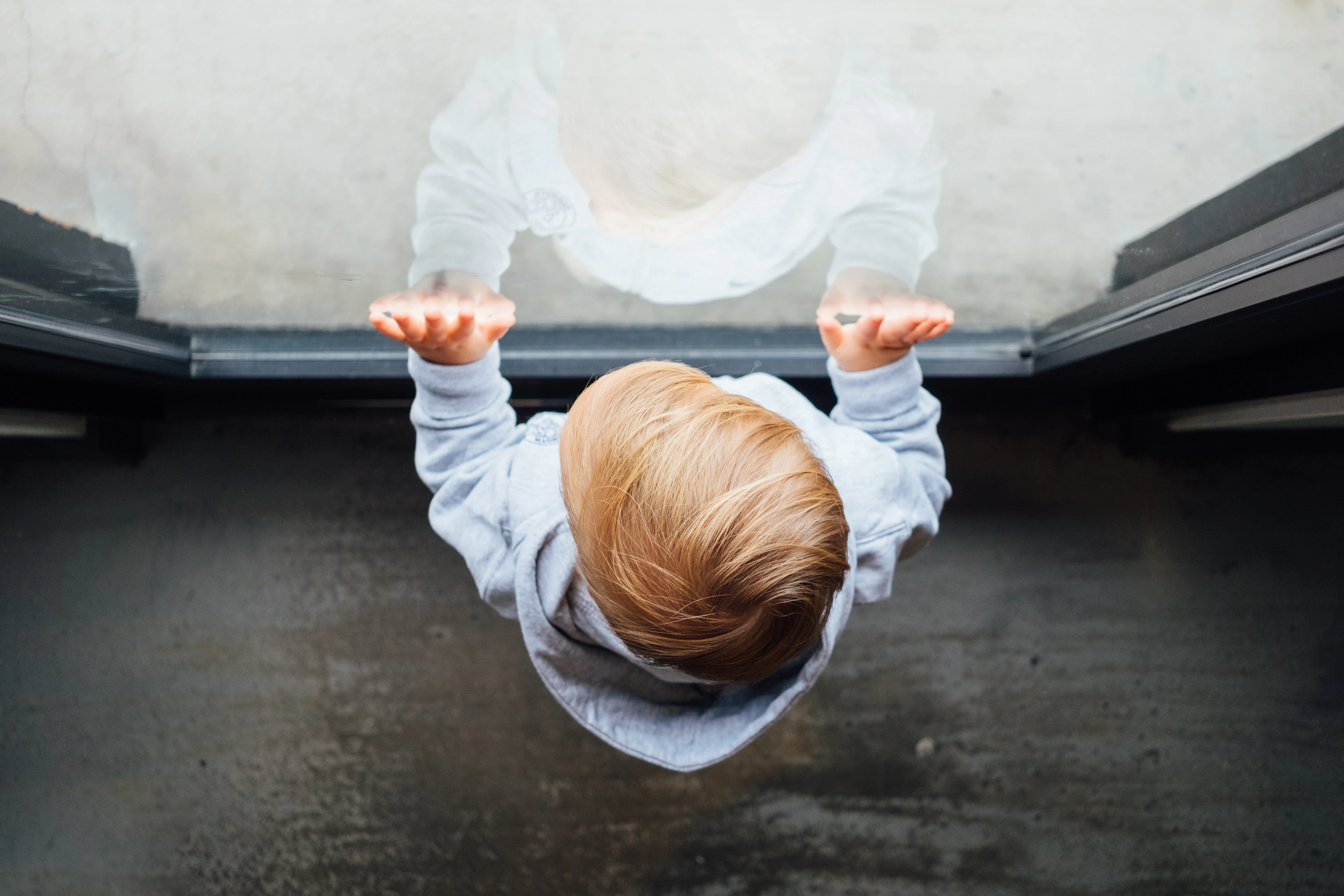 Young boy leaning on a glass door looking outside