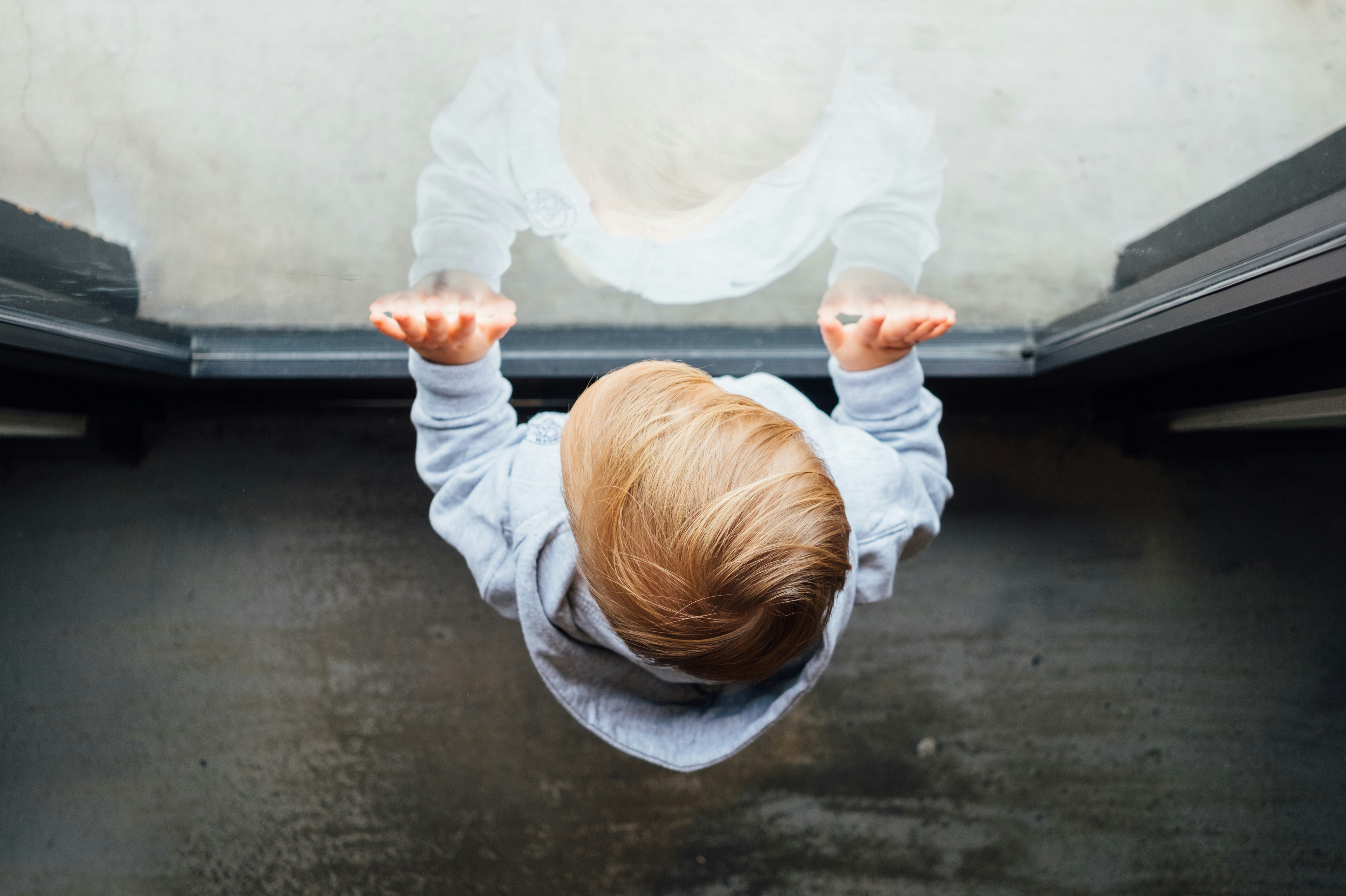 blonde haired boy in grey top leaning on glass door