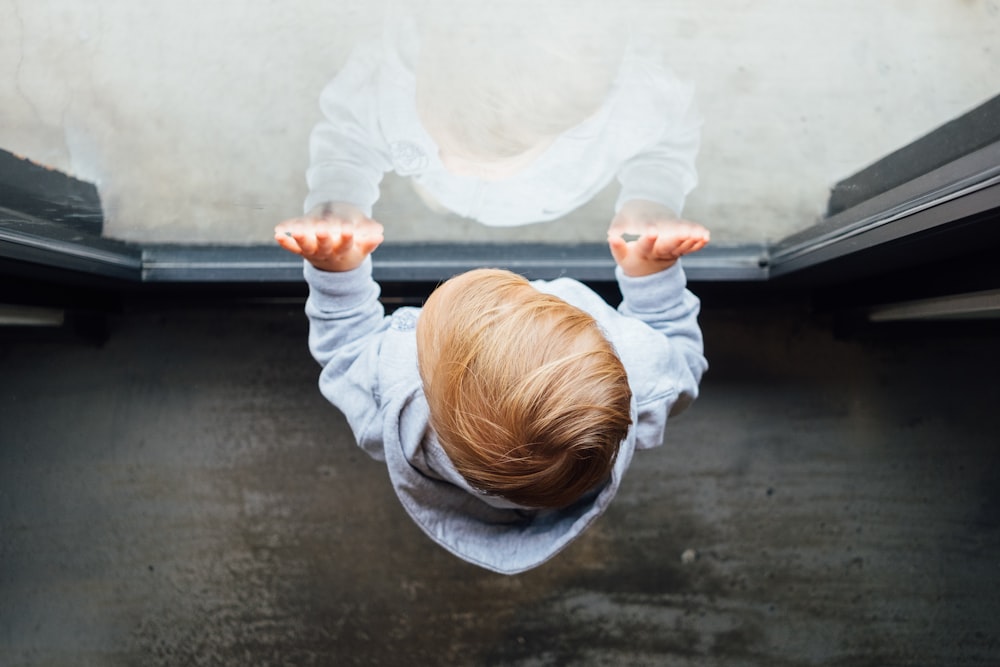 blonde haired boy in grey top leaning on glass door