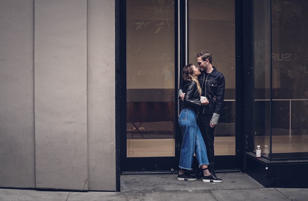 photo of man and woman kissing beside glass doors