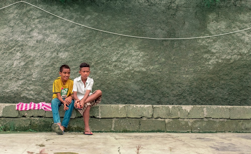 zwei Junge sitzen auf grauem Pflaster