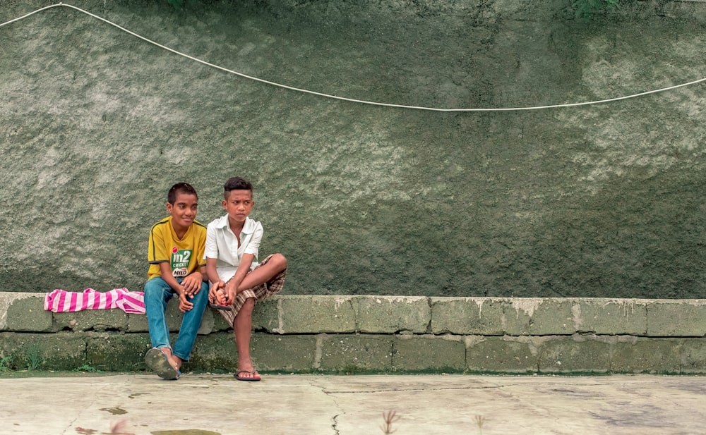 two boy sitting on gray pavement