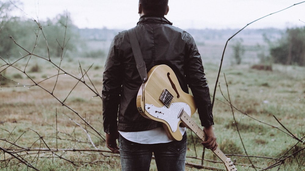 Hombre sosteniendo una guitarra marrón