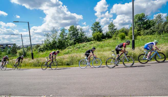 A group of cyclists riding past ancient temples and deer in Nara Park under a clear blue sky.