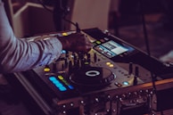 A person operates a DJ controller, adjusting the knobs and sliders on the equipment. The setup is illuminated by small, colorful LED lights, creating a vibrant and dynamic atmosphere.