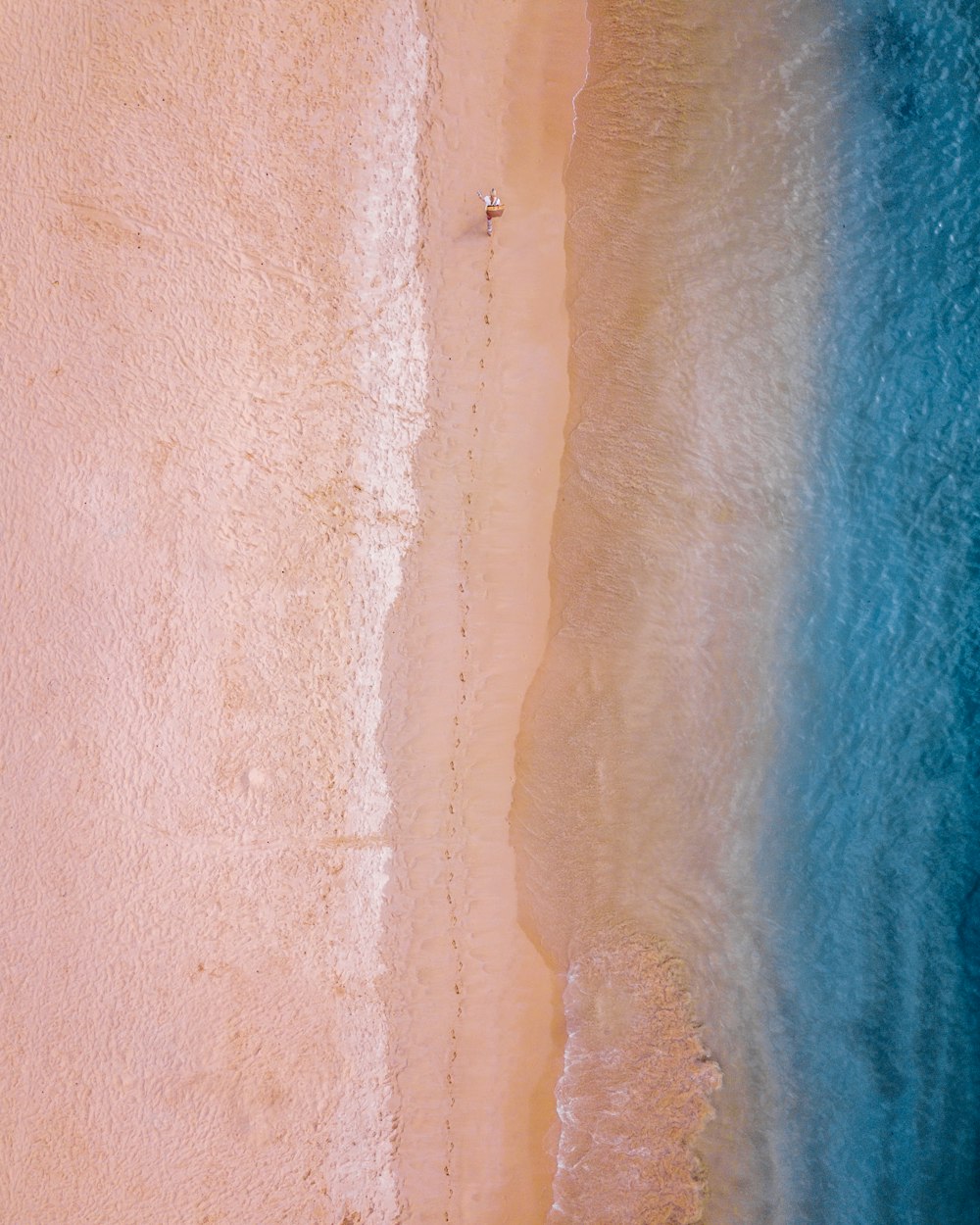 person walking on sand near seashore leaving foot trails