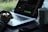 A person is using a laptop with a video editing software open on the screen. The workspace is minimalistic, featuring a smartphone and a mug with a black and white pattern. Natural light filters in, creating a serene atmosphere with greenery visible in the background.