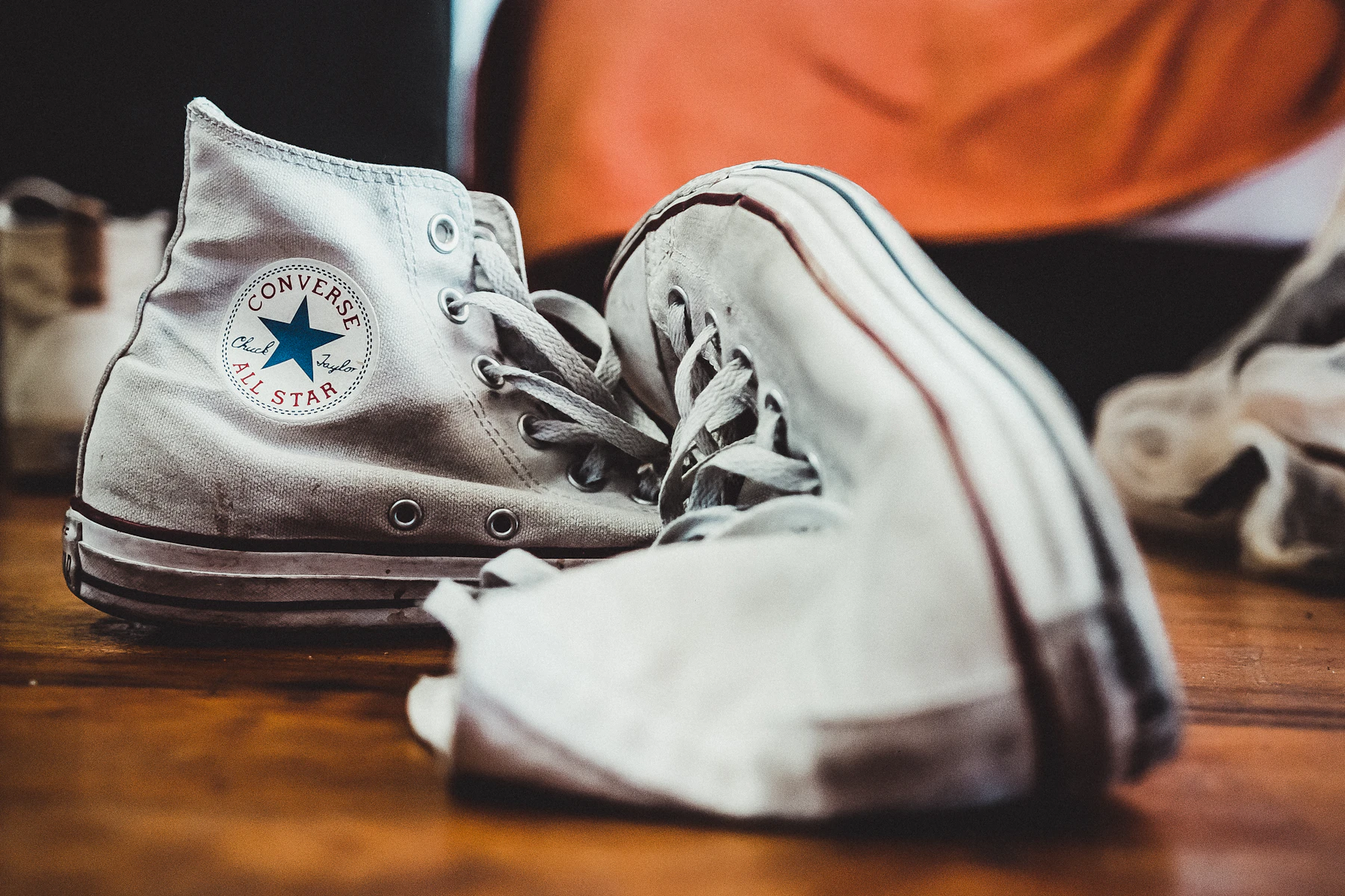 A worn pair of white canvas high-top sneakers on a wooden floor