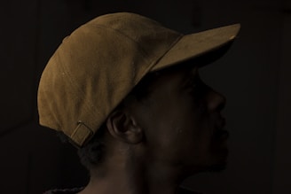 A person wearing a brown cap, captured in silhouette against a dark background. The contours of the face are slightly visible, with the focus on the texture and color of the cap.