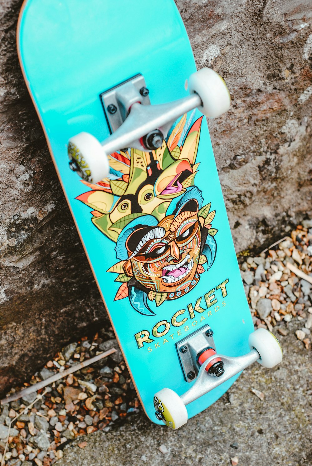 blaugrünes und mehrfarbiges Rocket Skateboard Grafik Skateboard tagsüber auf grauer Betonwand geparkt