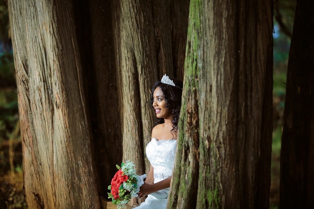 mulher vestindo vestido de noiva em pé segurando buquê entre árvores