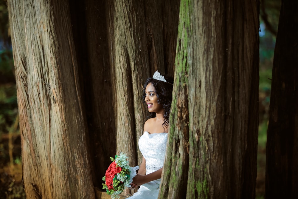 woman wearing wedding gown standing holding bouquet between trees