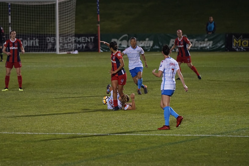 A dynamic action shot of a women's football player skillfully dribbling past defenders under stadium lights.
