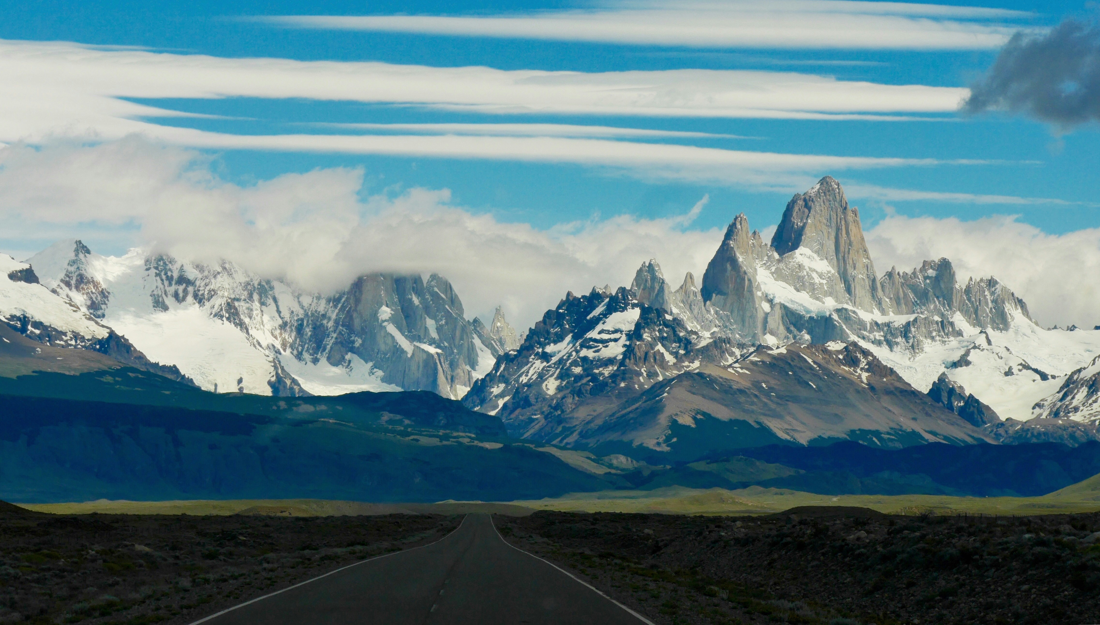 snow-covered mountain behind gray asphalt road, Road towards El Chalten Argentina