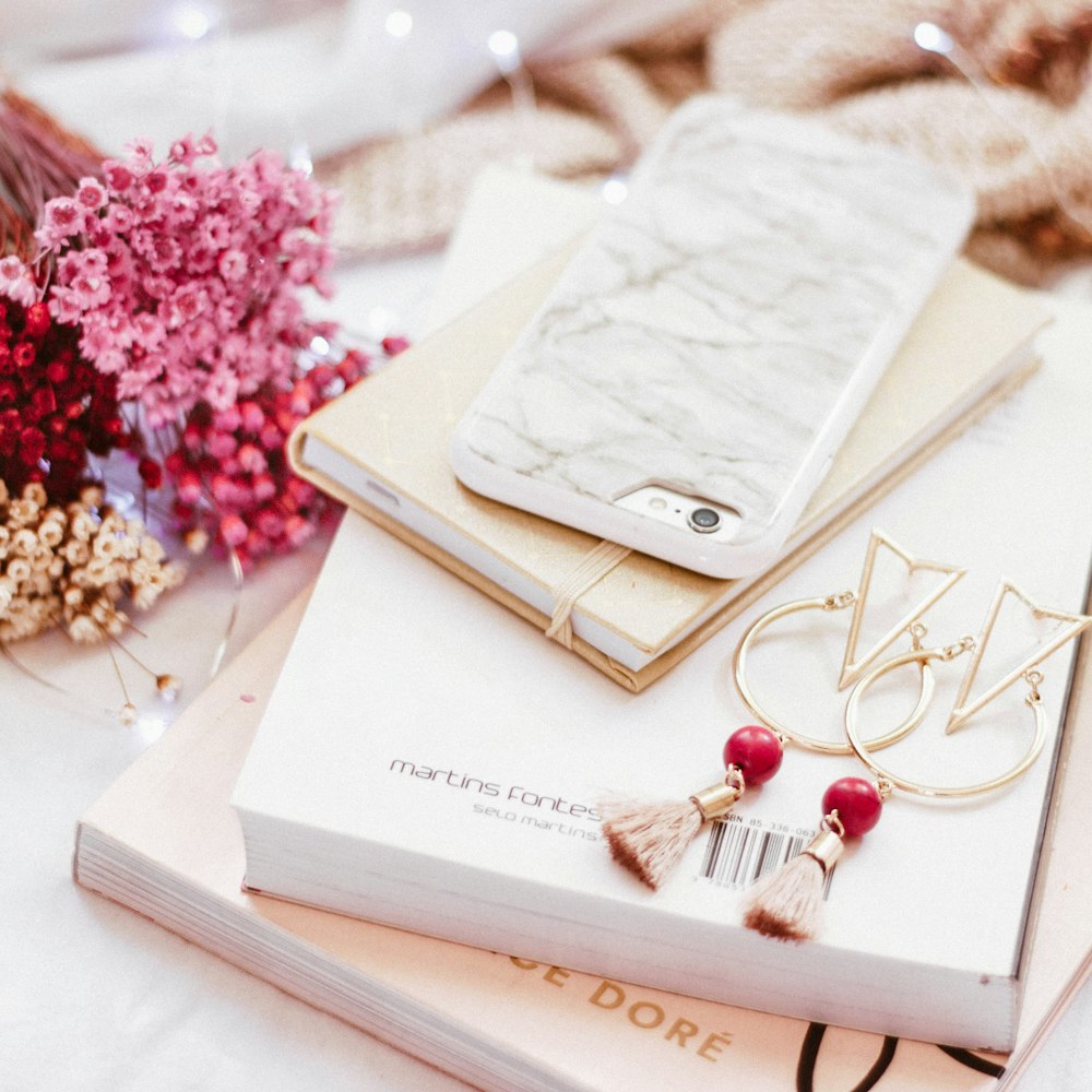 iPhone on book beside gold-colored earrings