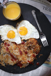 Cast iron breakfast of perfectly fried eggs with crispy edges alongside golden hash browns on a terra-cotta plate.