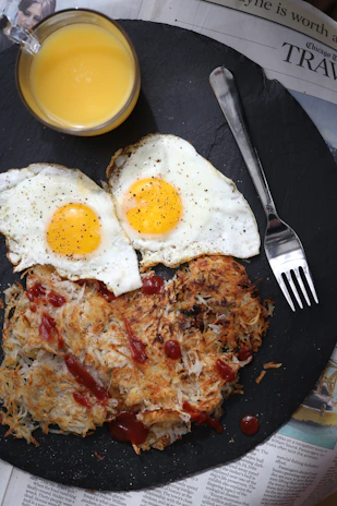 Cast iron breakfast of perfectly fried eggs with crispy edges alongside golden hash browns on a terra-cotta plate.