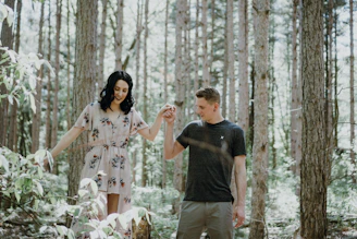 Boyfriend and girlfriend walking hand in hand along a sun-dappled forest path, smiling.