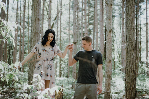 Boyfriend and girlfriend walking hand in hand along a sun-dappled forest path, smiling.