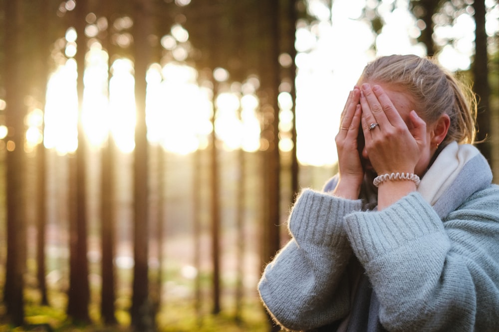 woman wearing gray coat with hands on her face during daytime