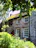A cozy sandstone cottage bathed in warm afternoon light, surrounded by lush greenery and rustic wooden shutters.