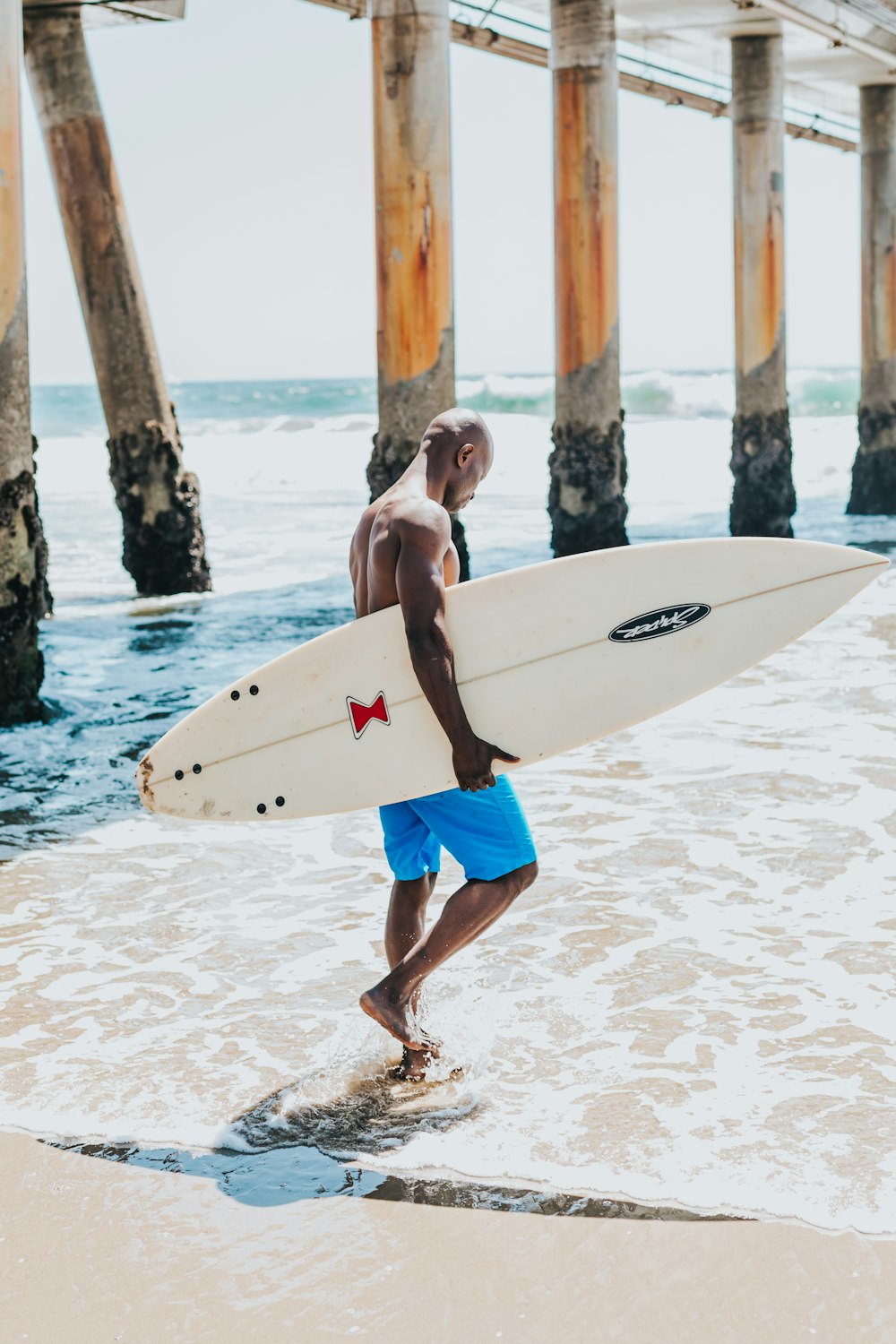 man holding white surfboard walking across ocean
