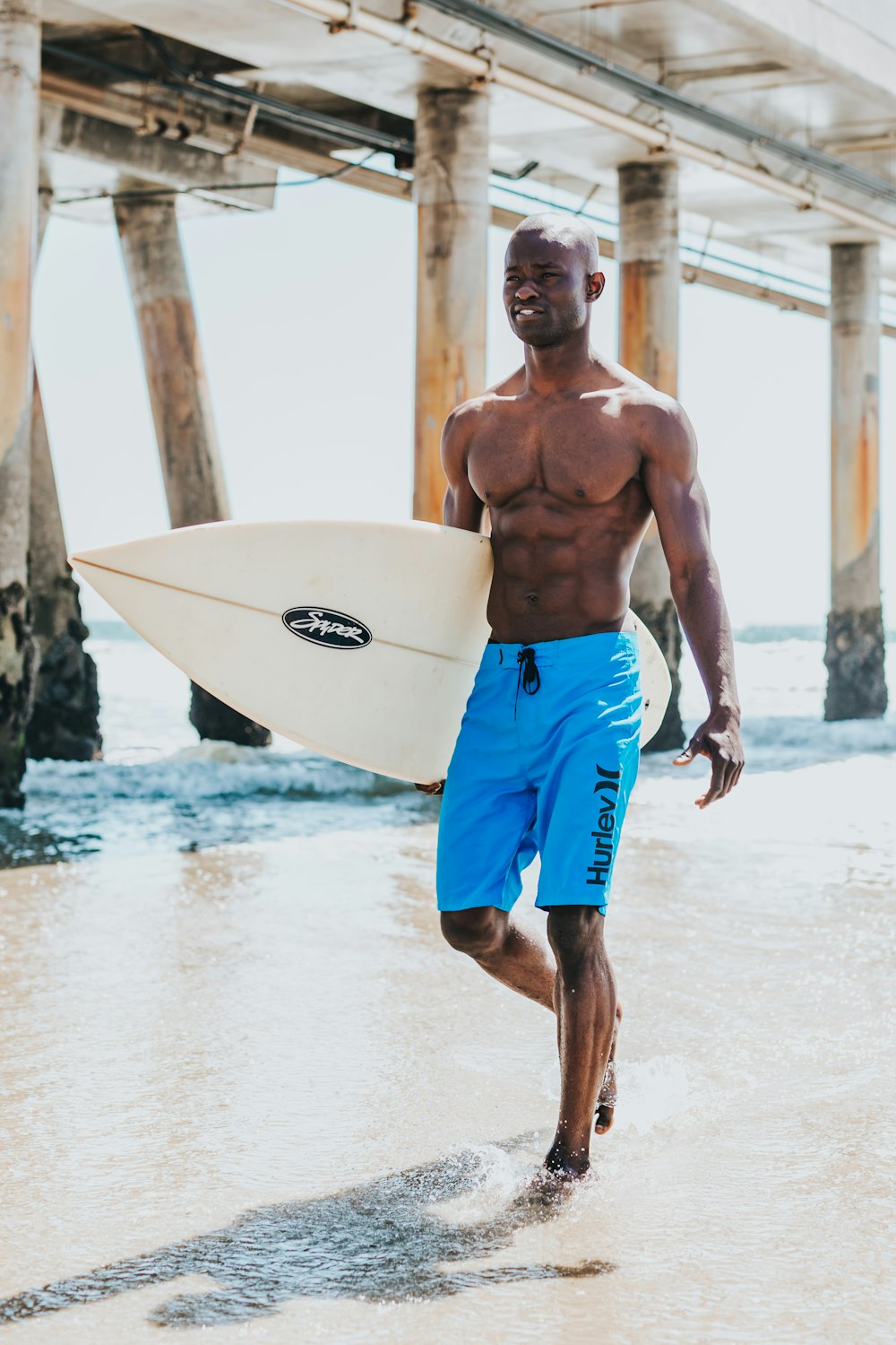 L’homme marche sur le bord de la mer avec une planche de surf pendant la journée