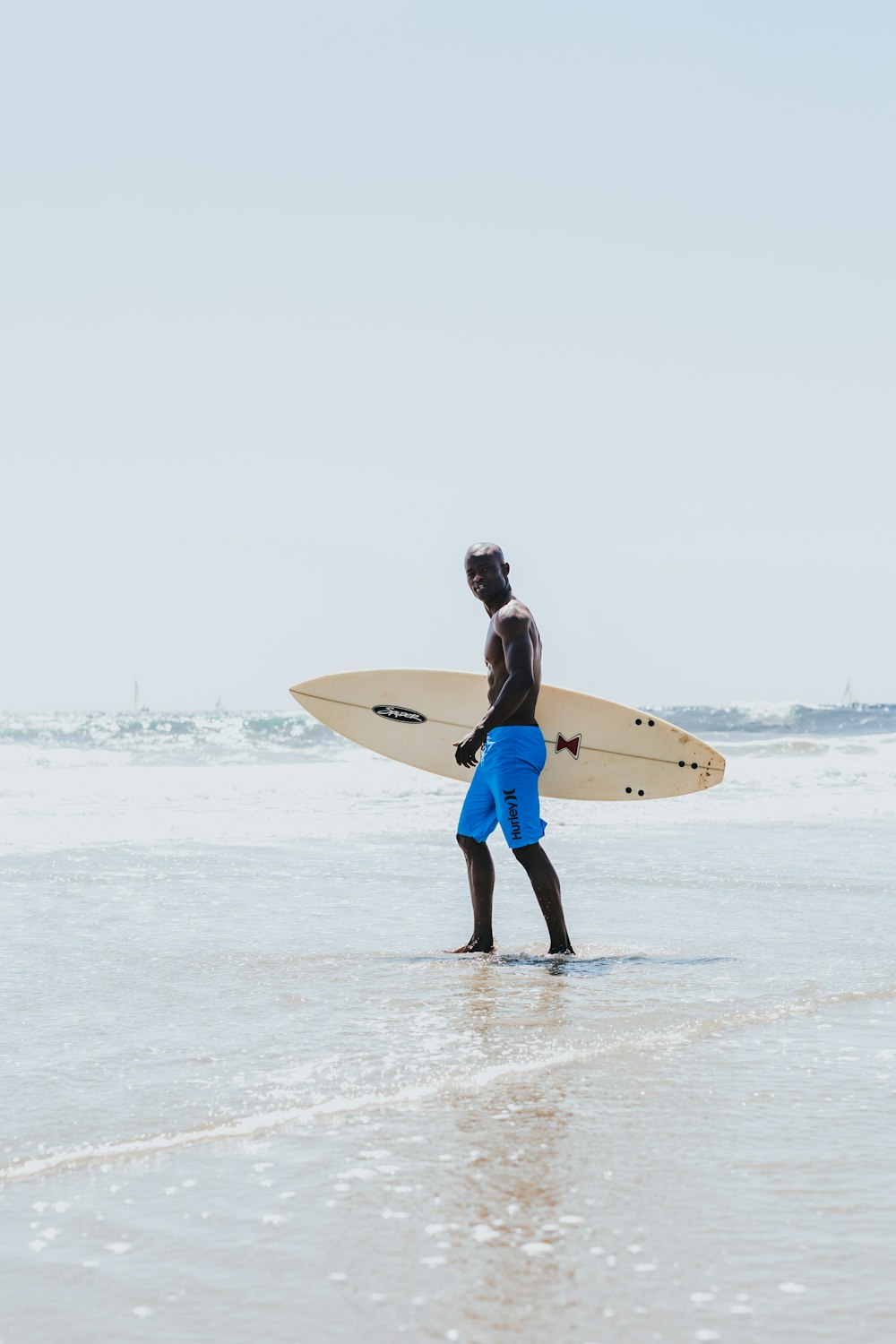hombre que lleva una tabla de surf de pie en la orilla