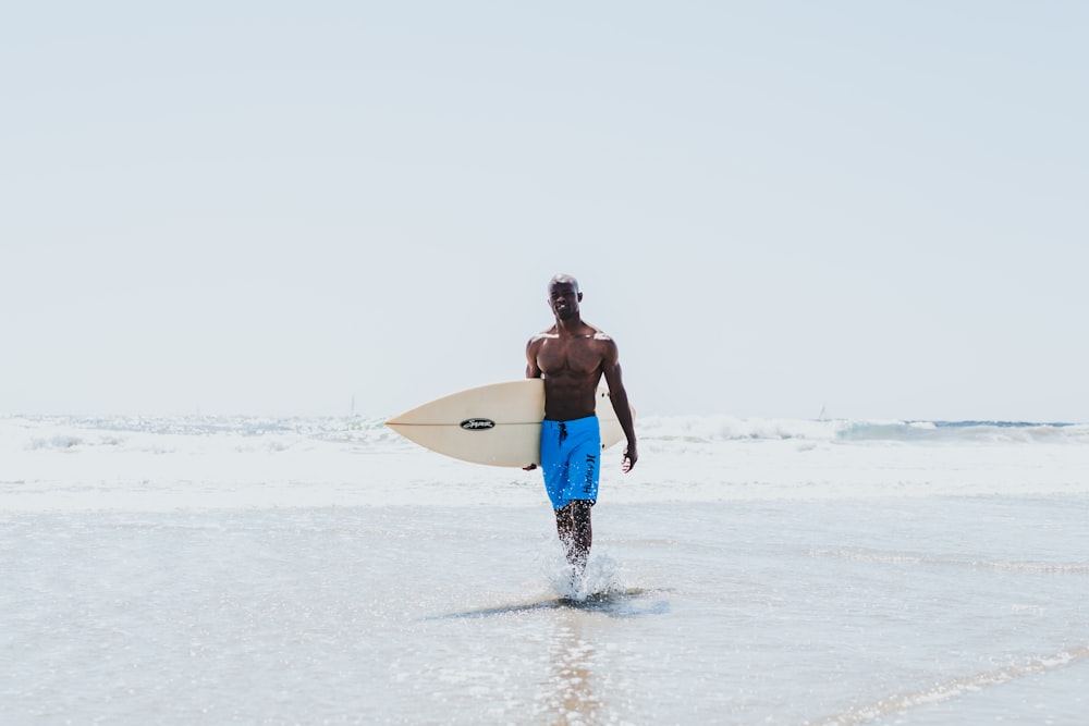 hombre caminando en la orilla del mar mientras sostiene una tabla de surf blanca