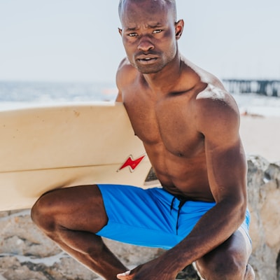 man sitting beside body of water holding white surfing board during daytime