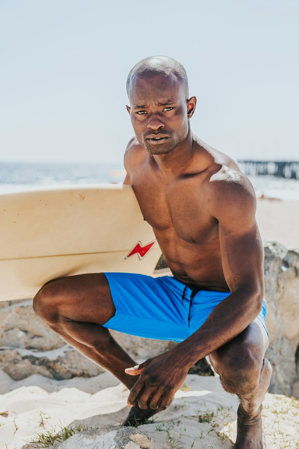 man sitting beside body of water holding white surfing board during daytime