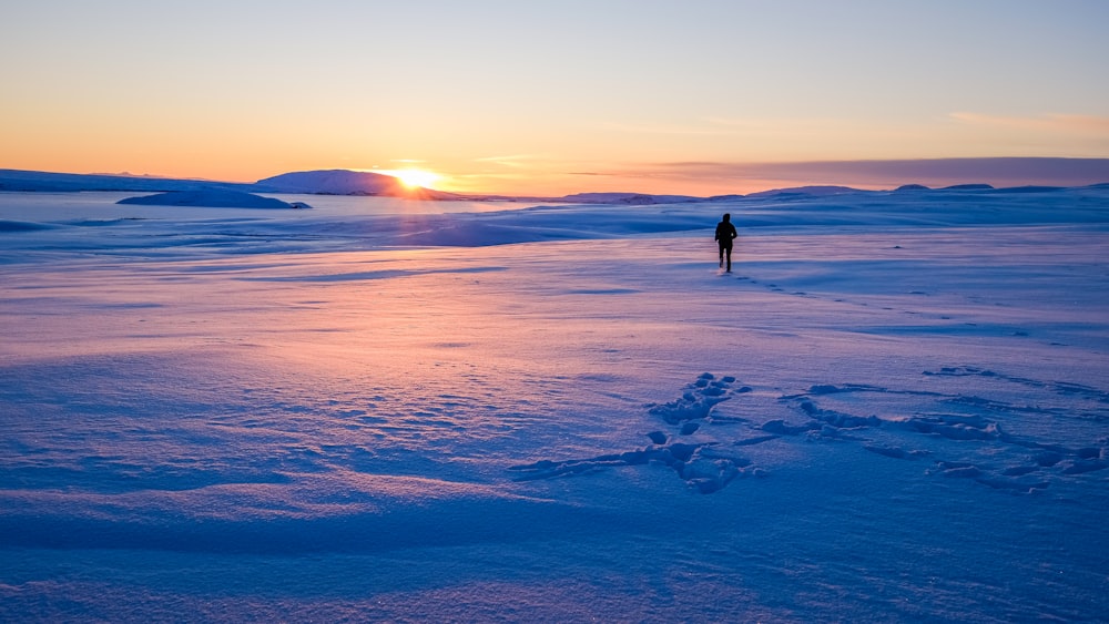 homem andando no campo de neve durante o nascer do sol
