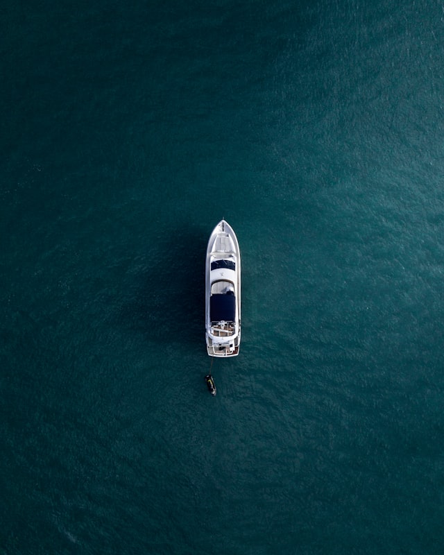Aerial view of a white luxury yacht gliding through calm turquoise waters on a sunny day