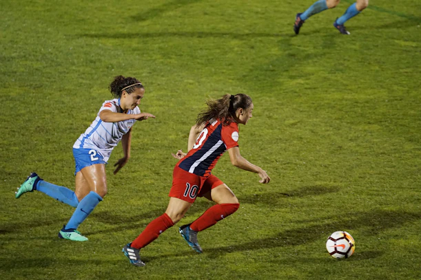 two women playing soccer on field