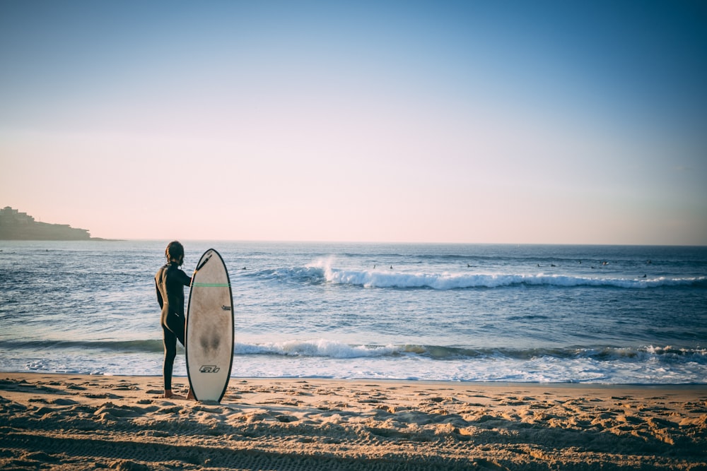 personne nue tenant une planche de surf sur le rivage de la plage