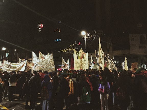 Evening scene of Iranian protesters with illuminated signs at a large public rally.