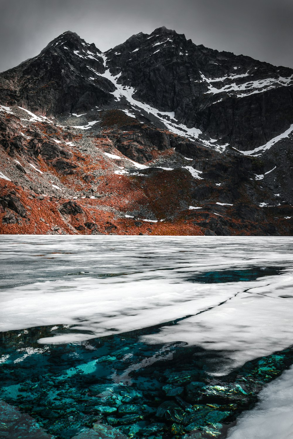 body of water near rocky mountain under gray sky