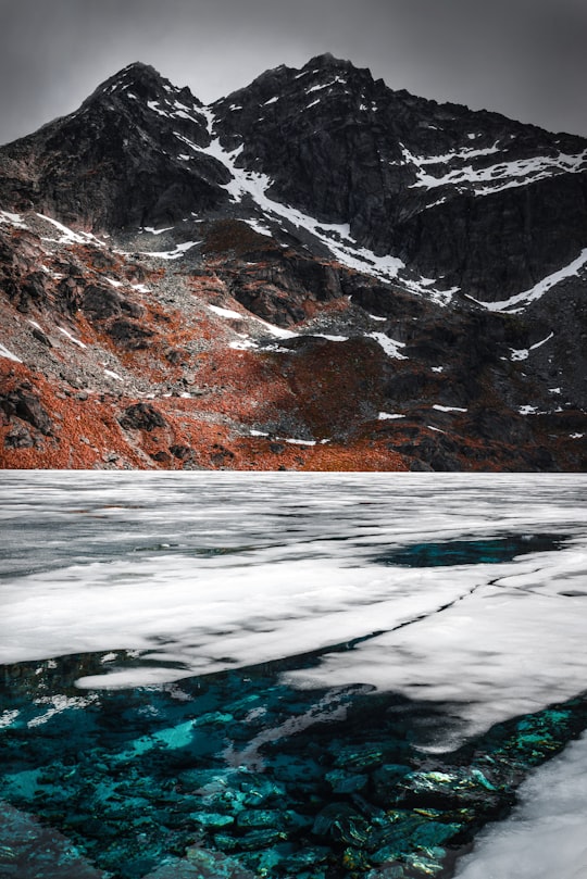 body of water near rocky mountain under gray sky in Lake Alta New Zealand