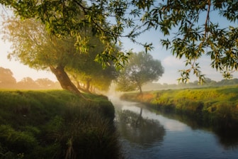 A serene river flowing through a lush green landscape at sunrise.