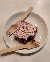 A close-up of a fork cutting into a moist red velvet cake with cream cheese frosting.