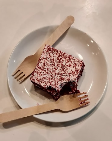 Close-up of a rich red velvet cake slice with creamy frosting on a pastel pink plate.