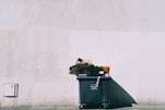 black plastic garbage bin with wheels beside wall